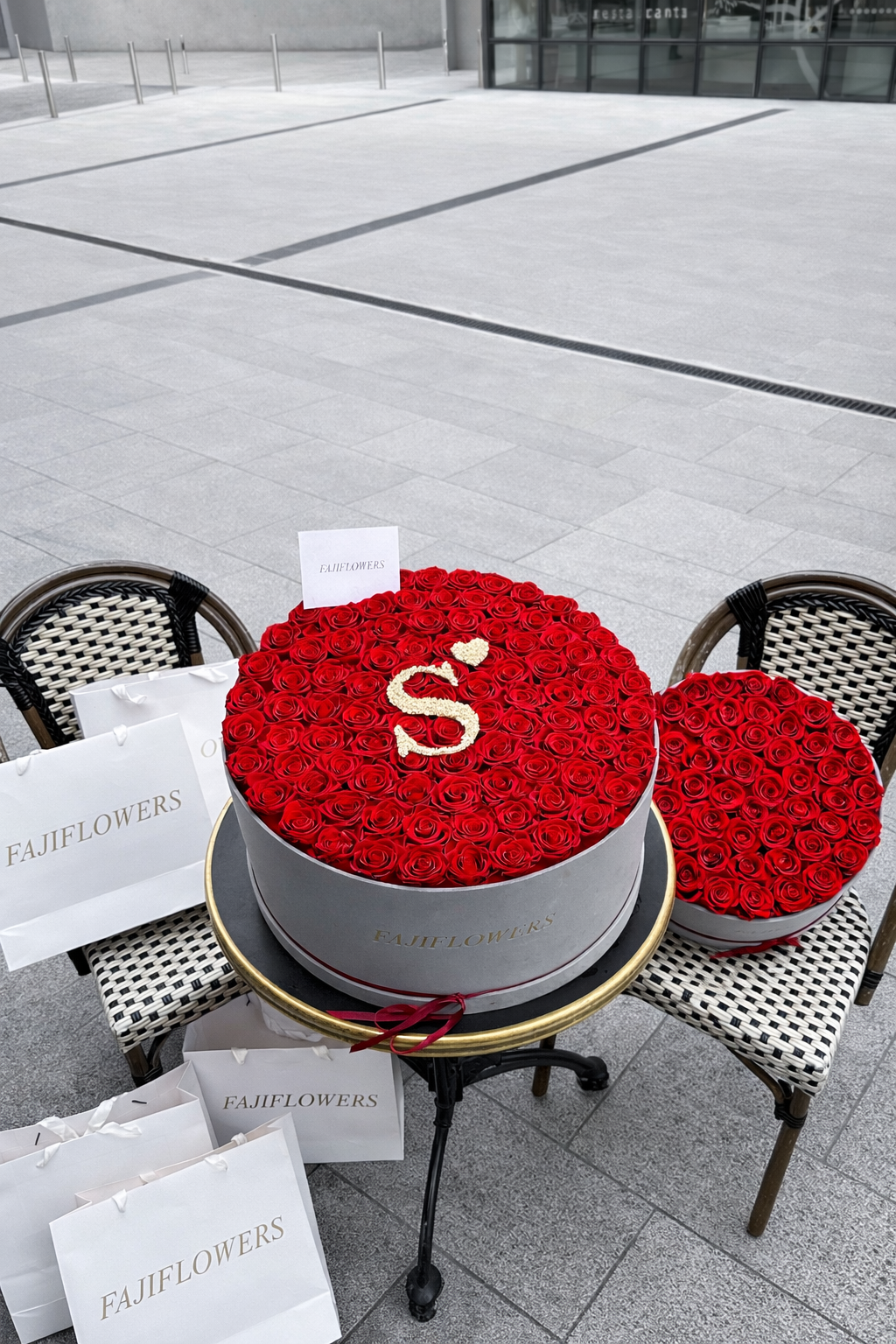 Grey FajiFlowers box of red roses with a white initial S on an outdoor café table.