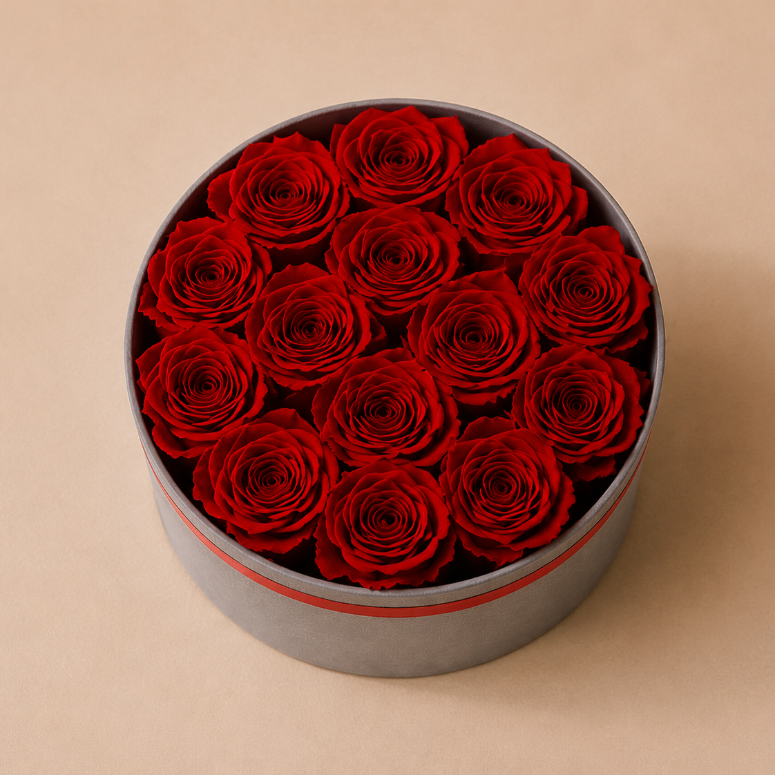 A round gray gift box filled with real preserved deep red roses, photographed from above on a warm beige background.